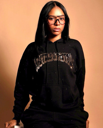 @yoselinpacheco394 in the Pastels & Pistols MotionDoLL Black Rhinestone Hoodie. Straight-on chest view highlighting chrome vinyl and rhinestones. Warm studio backdrop. Womens streetwear hoodie.
